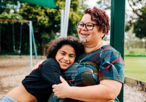 A young person and an adult embracing closely outdoors, both smiling