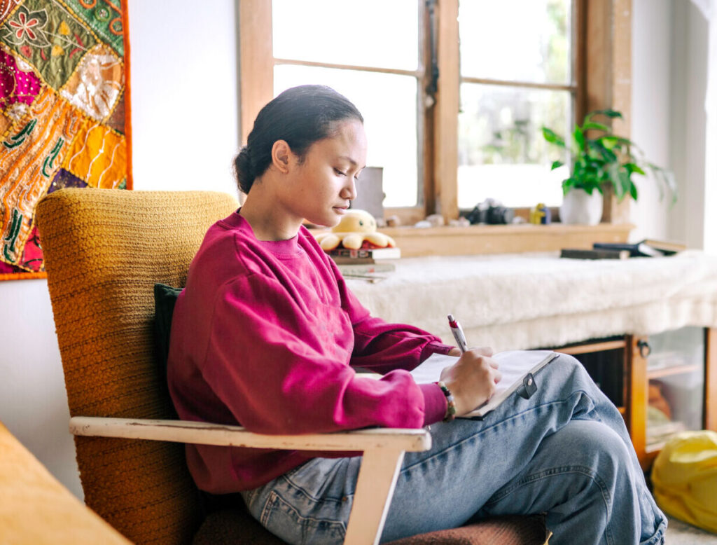 A person sitting by a sunlit window, writing or reading with focused attention