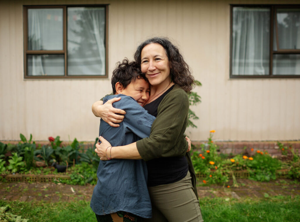 A woman and child embracing warmly outside a house, both smiling